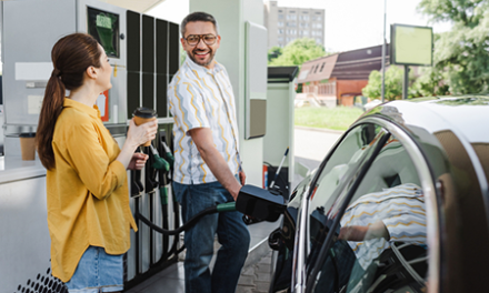 two people talk at gas station while one puts gas in car